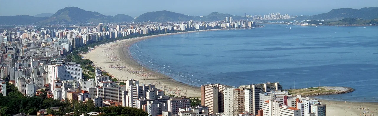 Vista aérea da orla de Santos, com a faixa de areia, os prédios e o mar.